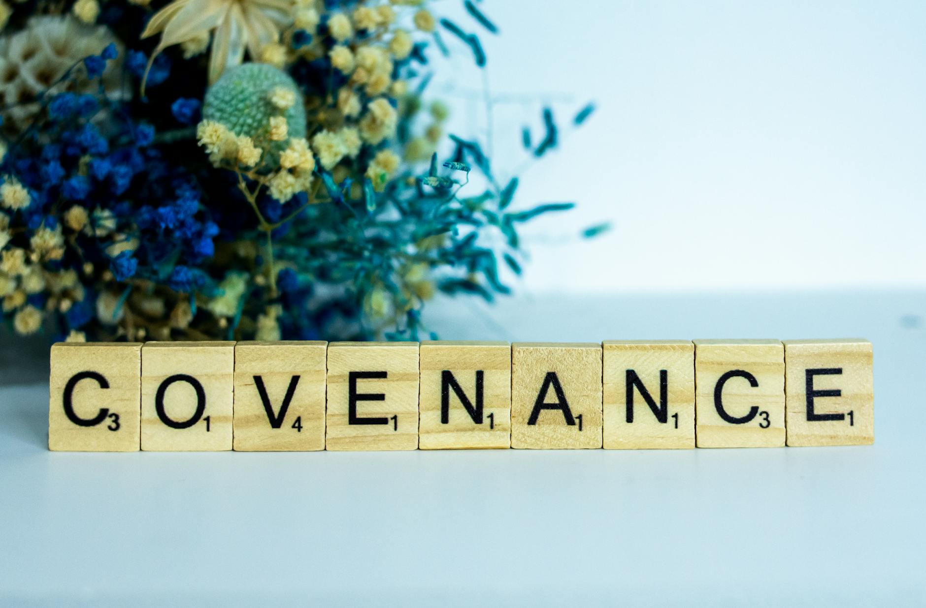 Drewniane kafelki Scrabble układające słowo Covenance na tle kwiatów