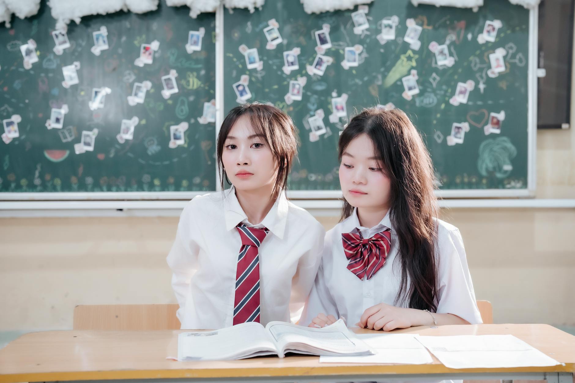 Dwójka uczniów w mundurkach siedzi przy ławce z książkami w klasie