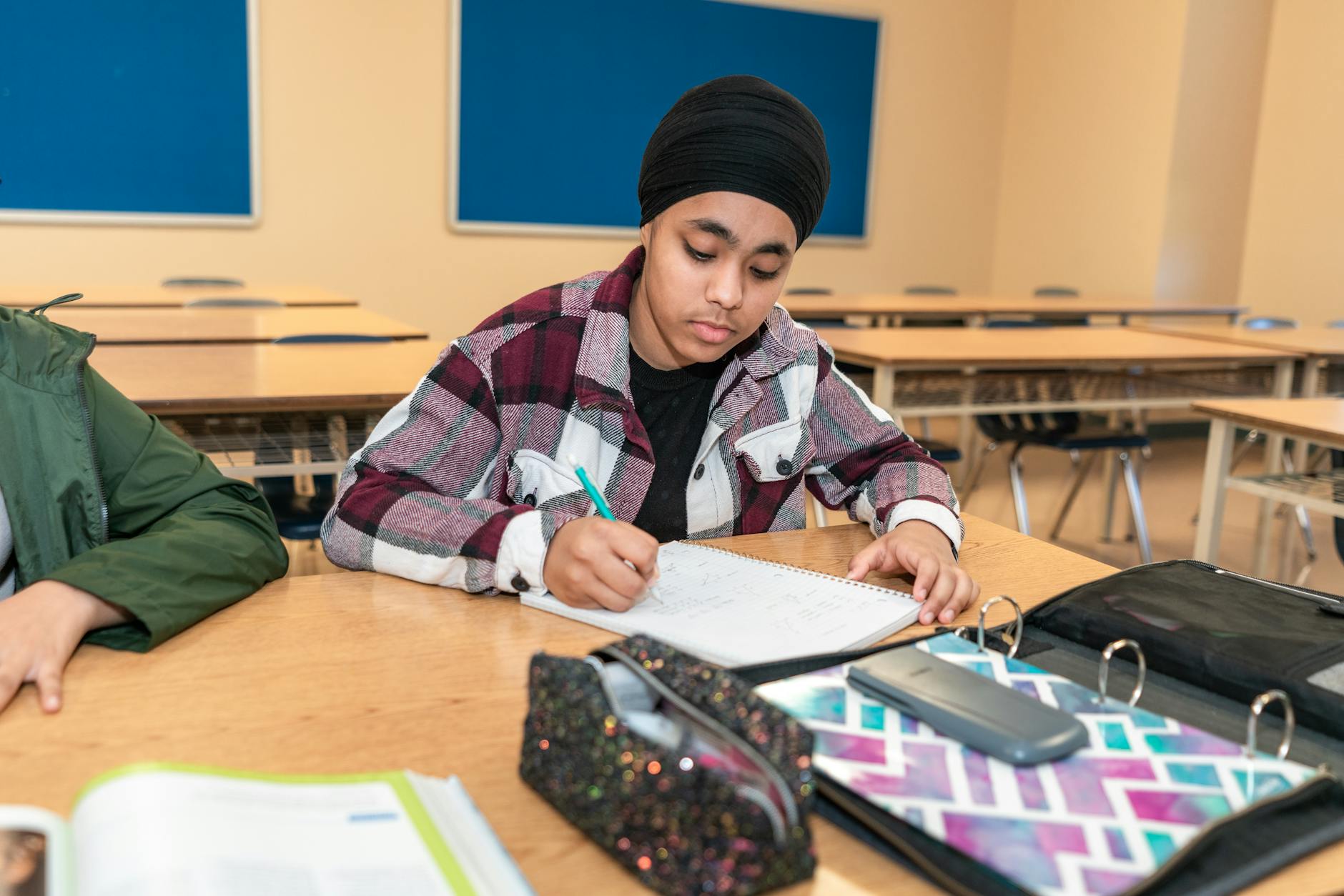 Uczeń z klasy 4–8 pisze przy ławce w sali podczas nauki